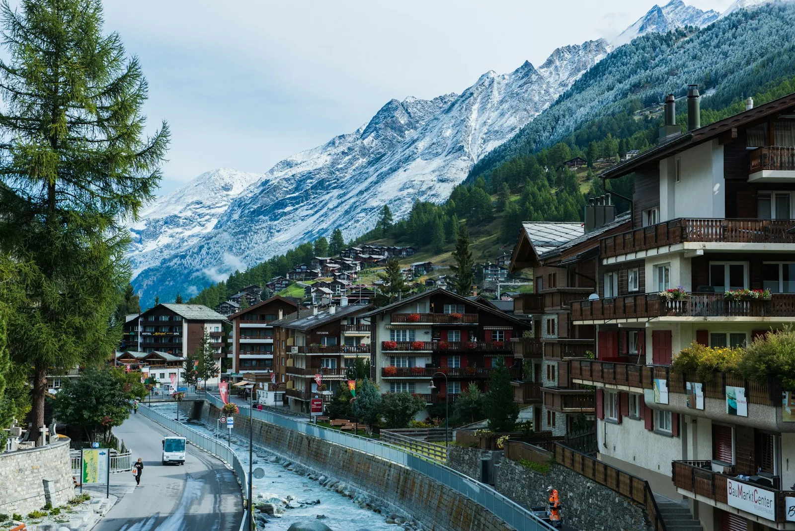 Traditional houses near a winding road with mountains and a blue sky in the background, showcasing the natural beauty of Switzerland.